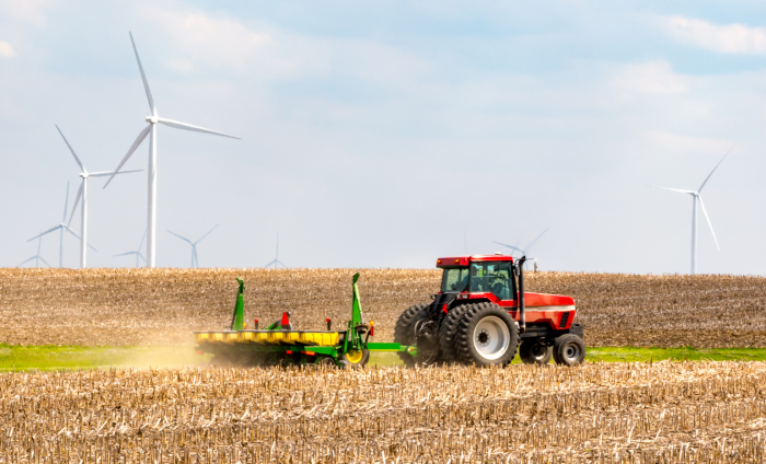 A tractor harvesting wheat, with wind turbines in the background.