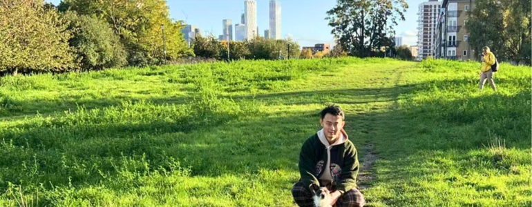 UCL School of Management Business Analytics MSc student Ruoyu Li posing with his dog to a background of UCL School of Management's Canary Wharf campus